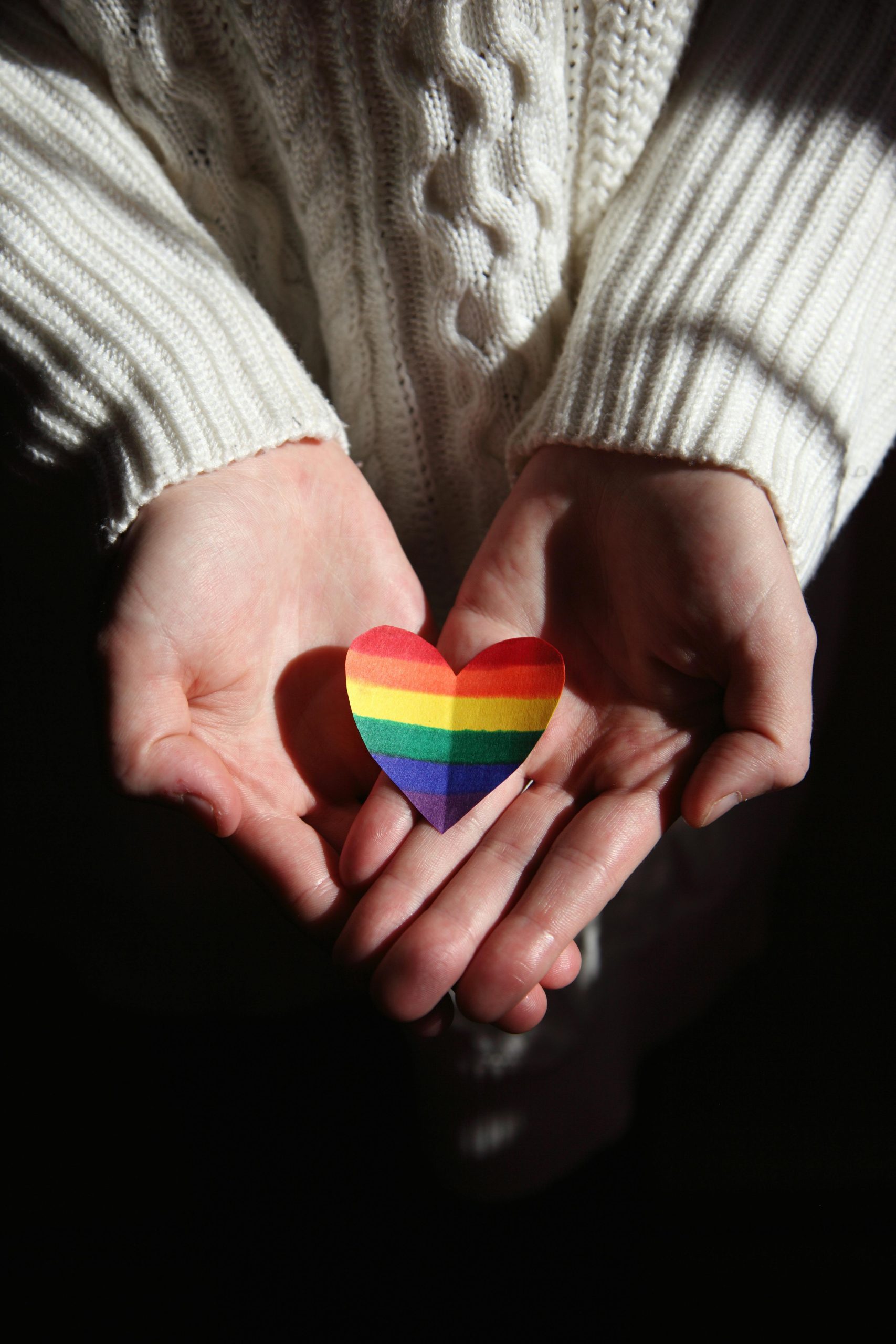 Close-up of hands cradling a rainbow heart, symbolizing love and LGBTQ+ pride.